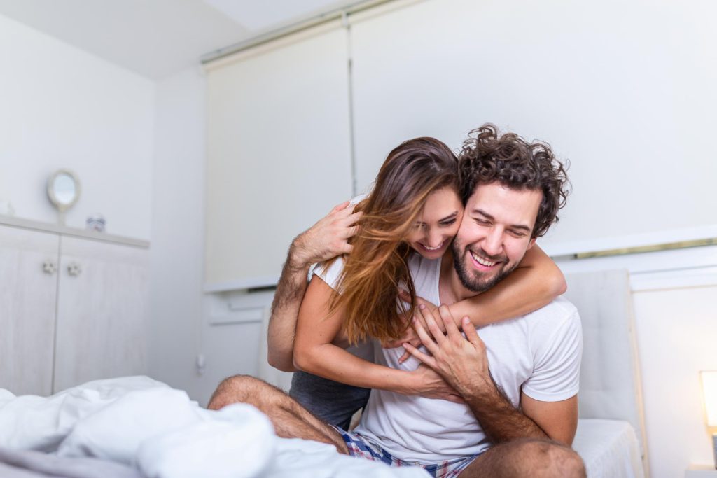 Nevető pár az ágyban, játékos ölelésben – eladó kamagra az önbizalomért